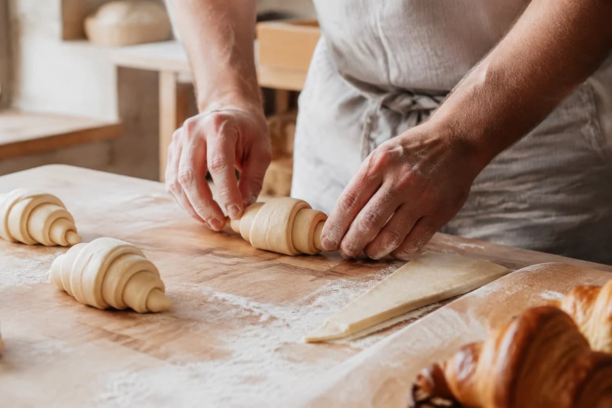 Flour-dusted hands shaping croissants on an oak workbench