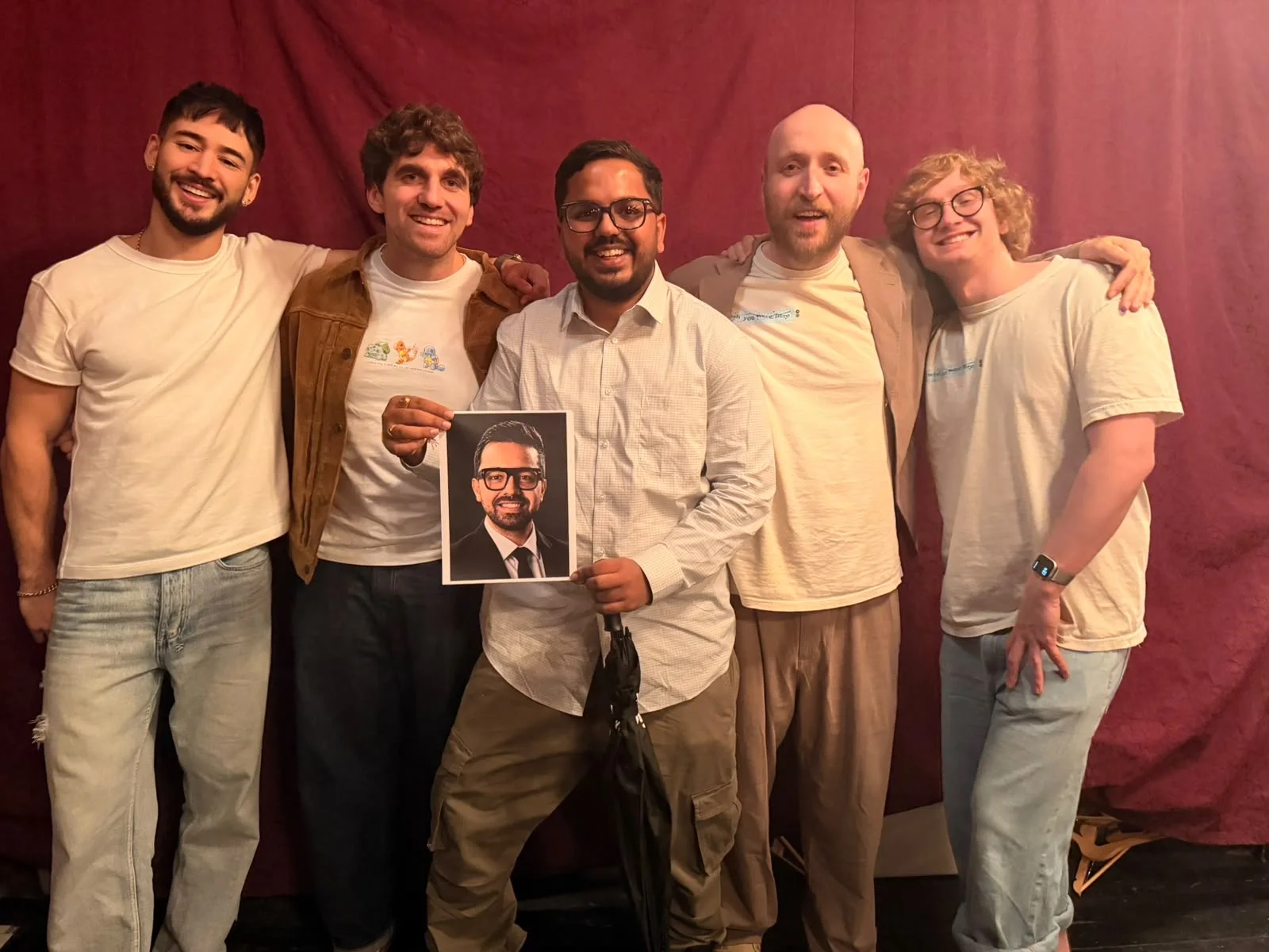 Utkarsh at Tech Roast Show in Montreal, holding a printed portrait of Parul in a group photo against red curtains.