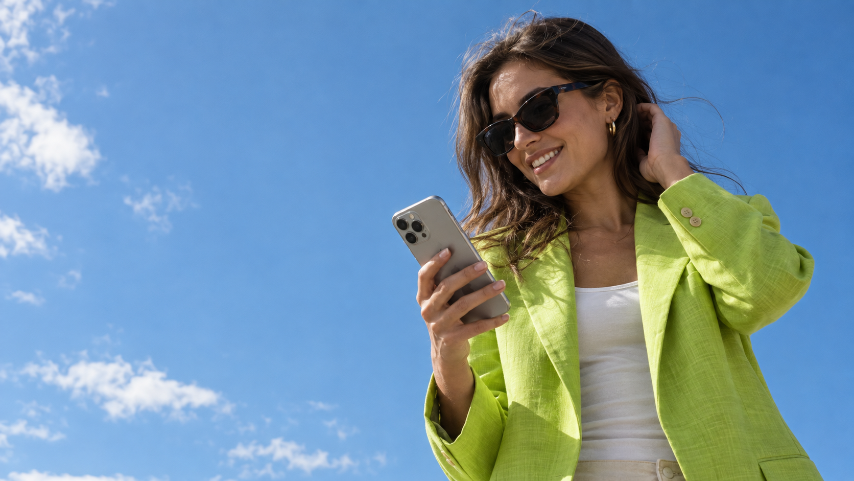 A creator in a lime linen blazer checking her phone beneath an open blue sky